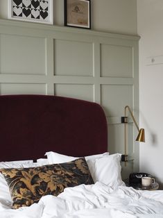 a bed with white sheets and pillows in a bedroom next to a wall mounted headboard