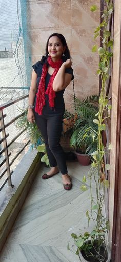 a woman standing on a balcony next to a potted plant and wearing a red scarf