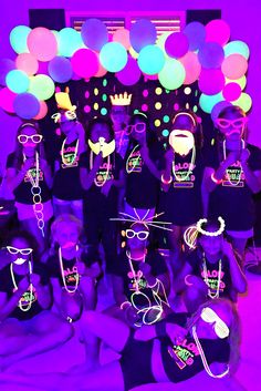 a group of people in black shirts and neon glasses posing for a photo with balloons