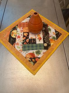 an orange vase sitting on top of a table next to a quilted place mat