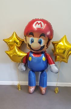 an inflatable mario balloon sitting on the floor with gold foil stars around it