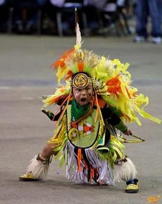 a man in an elaborate headdress and feathers is dancing on the street while people watch