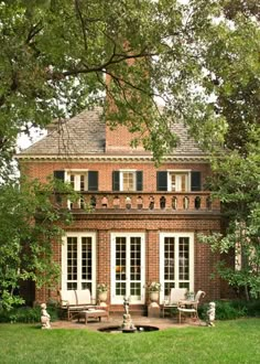 an old brick house with white windows and shutters on the front door is surrounded by lush green grass