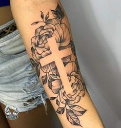 a woman's arm with flowers and a cross tattoo on the side of her arm