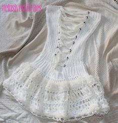 a white knitted top with lace and buttons on the bottom is laying on a bed