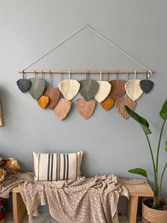 a wooden bench sitting in front of a wall hanging with different colored leaves on it