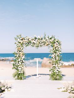 an outdoor wedding ceremony setup with white flowers and greenery on the aisle to the beach