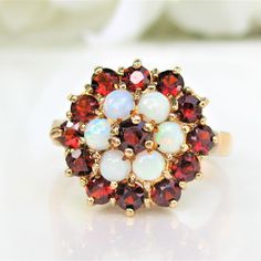 "A beautiful combination of garnet colored stones and opals presented in a \"Lady Di\" engagement ring style that is a stunner! The garnet center stone, is a prong set (one prong bent) round weighing approximately 0.10 carats encircled by 6 opals measuring approximately 0.10 carats each for a total of 0.60 carats. The bottom tier of gemstones consists of 12 additional garnet colored stones (loupe magnification shows one stone has edge chips) measuring approximately 0.07 carats each for another 0 Cluster Multi-stone Opal Ring For Anniversary, Unusual Engagement Rings, Halo Wedding Ring, Beautiful Rings Vintage, Bridal Jewelry Vintage, Alternative Engagement Ring, Wedding Rings Halo, Etsy Wedding Rings, Colored Stones