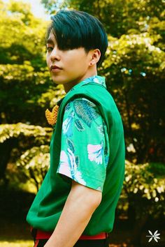 a young boy wearing a green shirt and red shorts standing in front of some trees