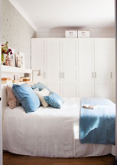 a bed with blue and white pillows on top of it next to a wall mounted cabinet