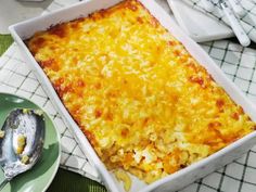 a casserole dish with cheese on top next to a plate and spoons