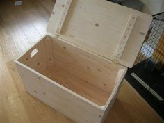 an open wooden box sitting on top of a hard wood floor next to a cage