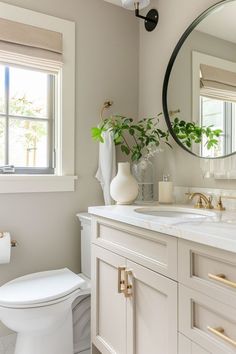 a white toilet sitting next to a bathroom sink under a round mirror in a bathroom