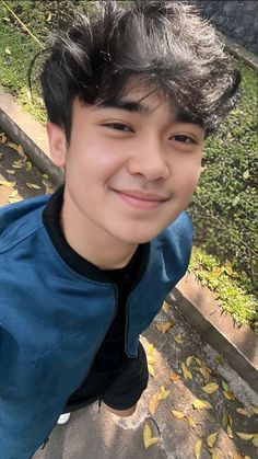 a young man smiling at the camera with leaves on the ground in front of him