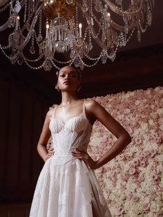 a woman standing in front of a chandelier wearing a white dress with flowers on it