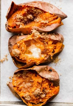 three baked sweet potatoes sitting on top of a white tray with crumbled toppings