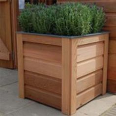 a wooden planter filled with green plants on top of a stone floor next to a building