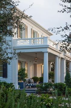 a large white house with columns on the front porch and covered in blue furniture, surrounded by greenery