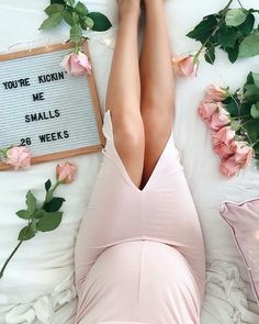 a woman laying on top of a bed next to flowers and a sign that says you're kiddin me smalls 28 weeks