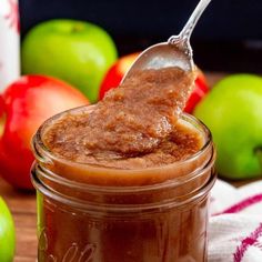 a spoon full of caramel apple butter on a wooden table with apples in the background