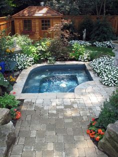 an outdoor hot tub surrounded by flowers and rocks