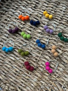 several different colored pom - poms are hanging from hoop earrings on a wicker surface