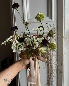 a person holding a bouquet of flowers in front of a door with a ribbon tied around it