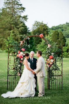 a bride and groom standing in front of an iron arch with flowers on it at their wedding