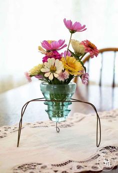 a glass vase filled with colorful flowers on top of a doily covered dining room table