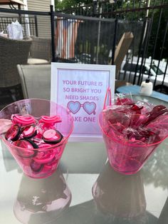 two pink cups filled with candy sitting on top of a table next to a sign