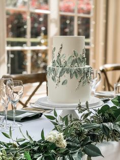 a wedding cake sitting on top of a table next to wine glasses and greenery