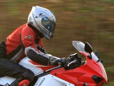 a man riding on the back of a red and white motorcycle down a road with trees in the background