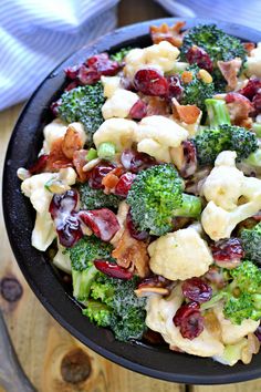 a bowl filled with broccoli and cranberries on top of a wooden table