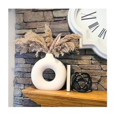 a white vase sitting on top of a wooden mantle next to a clock and other items