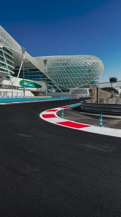 an empty race track in front of a large building with a curved roof and colorful lines on the side