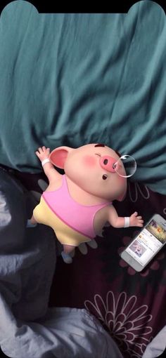 a little pig laying on top of a bed next to a cell phone