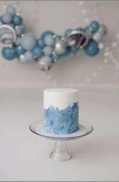 a blue and white cake sitting on top of a glass plate next to some balloons