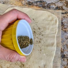 a person is sprinkling seeds in a yellow cup on a floured surface