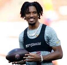 a man with dreadlocks holding a football in his hand and smiling at the camera