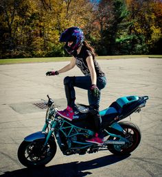 a woman riding on the back of a blue and pink motorcycle in a parking lot