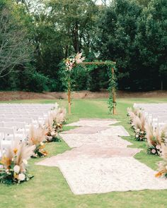 an outdoor ceremony setup with white chairs and flowers on the aisle, surrounded by greenery