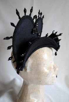 The Queen of Darkness headdress is a glorious Tudor inspired attifet headdress with a gothic twist!This vampire style headdress is covered with black silk shantung and embellished with black cord trimming all around the edges.It is further trimmed with black crystal details that create a halo effect. The piece is completed with a black crystal handmade elements placed at the center of both at the frond as well as the back part,to add that extra drama that we all love! The base is a headband styl Black Fantasy Costume Accessories For Theater, Black Punk Costume Hats And Headpieces, Black Fantasy Costume Accessories For Carnival, Gothic High Crown Headpiece For Costume Party, Black Fitted Fantasy Costume Hats And Headpieces, Steampunk Halloween Festival Headpiece, Gothic High Crown Costume Headpiece, Black Fantasy Costume Accessories For Festival, Black Fantasy Festival Costume Accessories