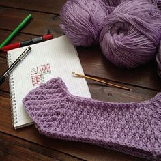 a crochet hat and yarn next to a notebook on a wooden table with markers