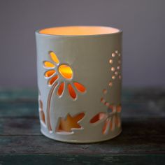 a white candle holder with an orange flower design on the front and side, sitting on a wooden table