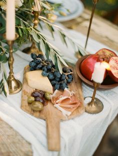 an assortment of cheeses, meats and fruit on a wooden cutting board with candles