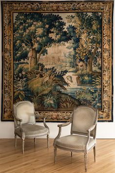 two chairs sitting next to each other in front of a wall hanging with a tapestry