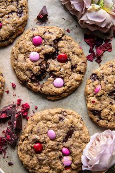 chocolate chip cookies with pink and red candies are on a baking sheet next to flowers