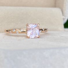 a pink diamond ring sitting on top of a white velvet box with diamonds around it