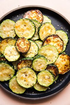 cooked zucchini slices in a black plate on a pink tablecloth with sprinkled parmesan cheese