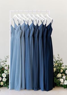 four bridesmaid dresses hanging on a rack in front of flowers